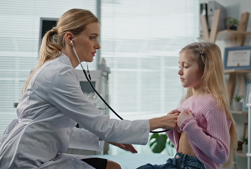 Детский врач-кардиолог на приёме внимательно слушает сердце ребёнка в комфортном кабинете клиники