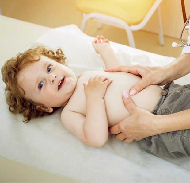 Мальчик сидит на кушетке в медицинском центре, врач-гастроэнтеролог с доброй улыбкой проводит осмотр живота.